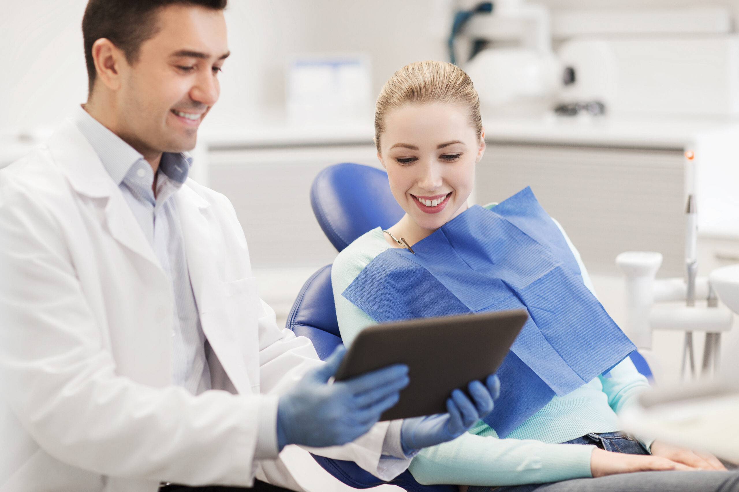 people, medicine, stomatology and health care concept - happy male dentist showing tablet pc computer to woman patient at dental clinic office