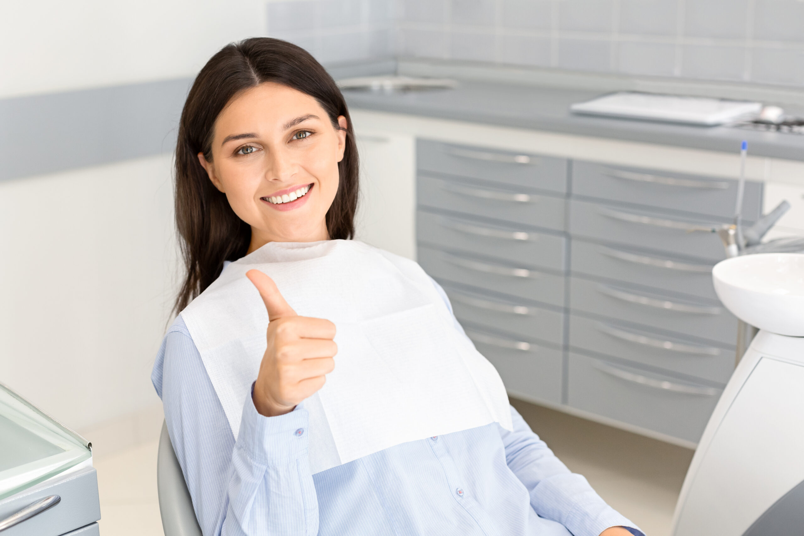 Portrait of pretty brunette female patient smiling and showing thumb up in dentistry, free space