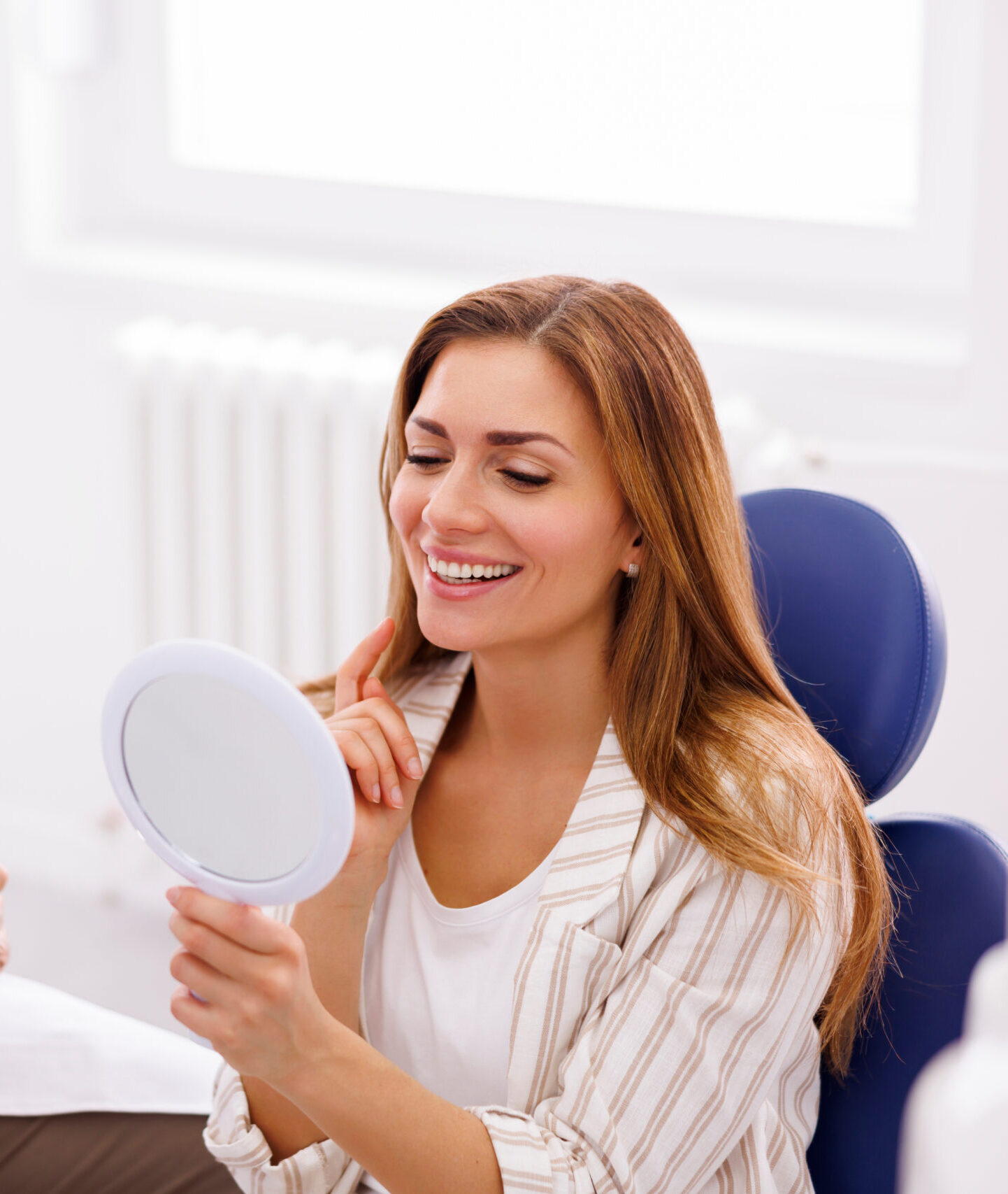 Woman looking in the mirror and smiling after checkup at dentist office; dentist and patient at dental clinic
