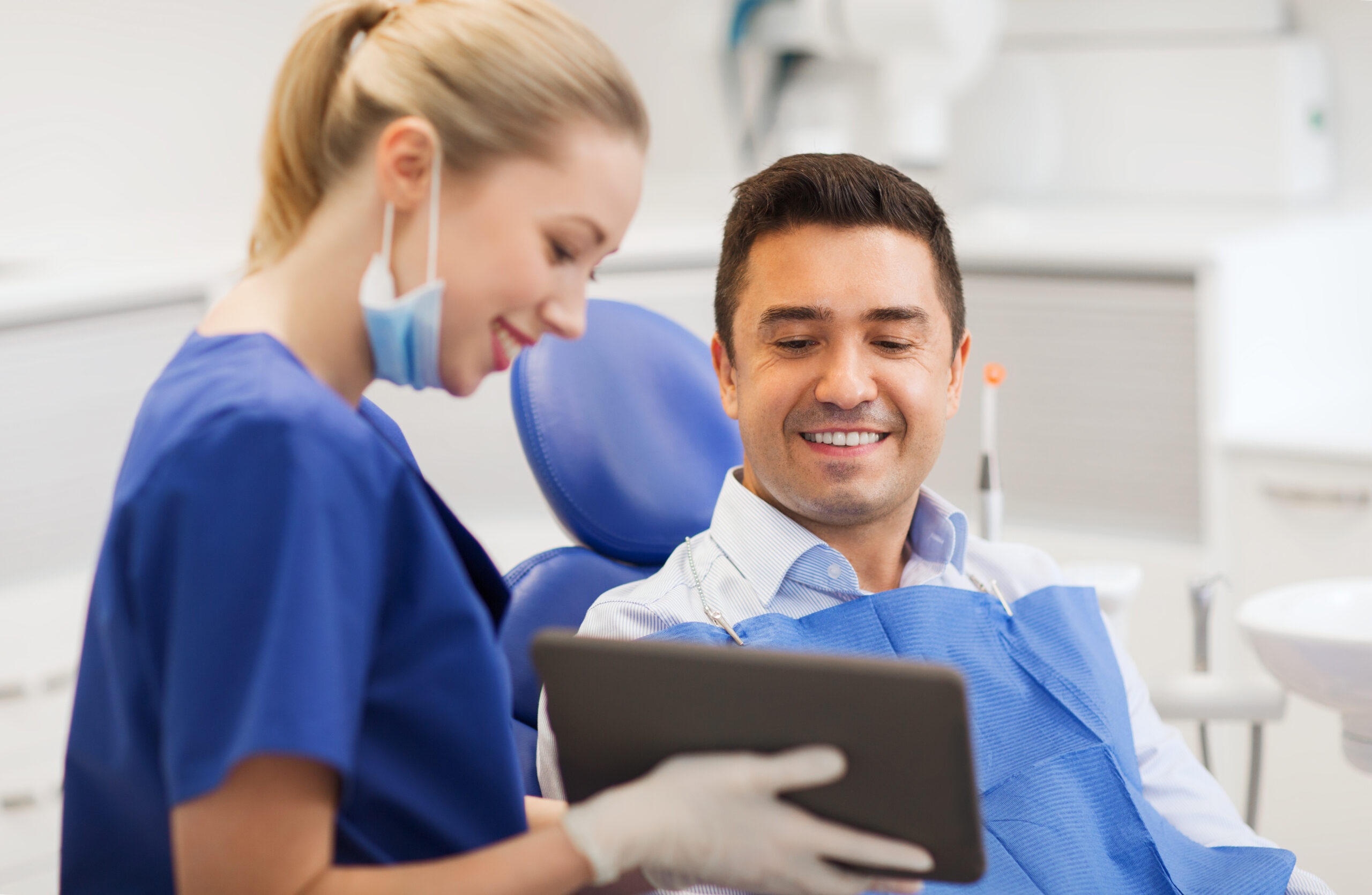 people, medicine, stomatology and health care concept - happy female dentist showing tablet pc computer to male patient at dental clinic office