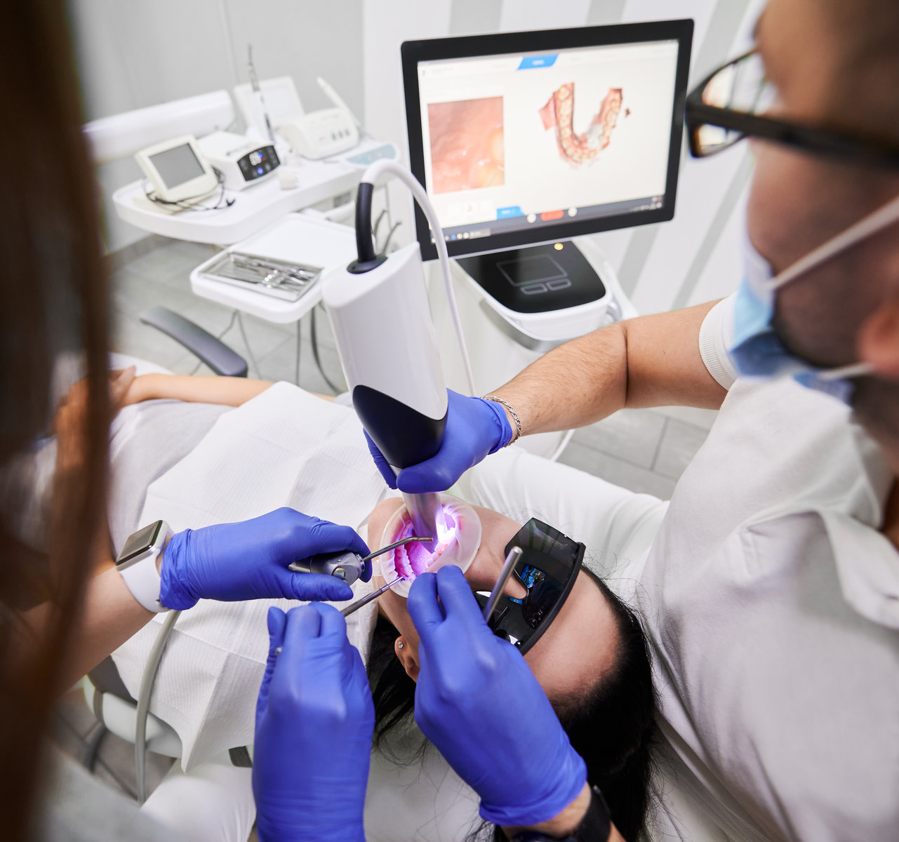 Dentist and assistant using intraoral scanner while examining patient teeth in dental office. Dental specialist performing intraoral scanning with modern scanning machine. Concept of digital dentistry
